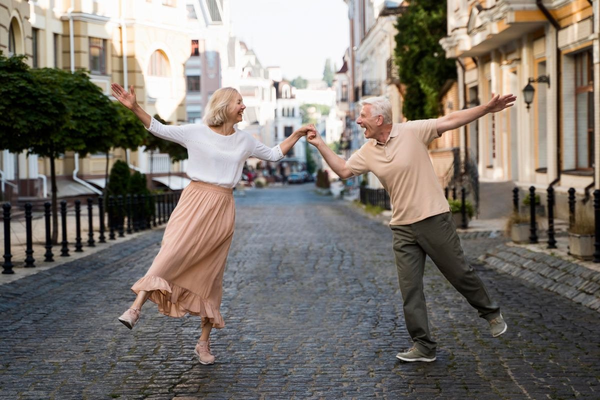 Older couple joyfully dancing and holding hands on a cobbled street in a charming historic town