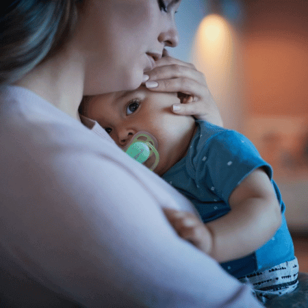 Mother and baby cuddling. Baby using soother