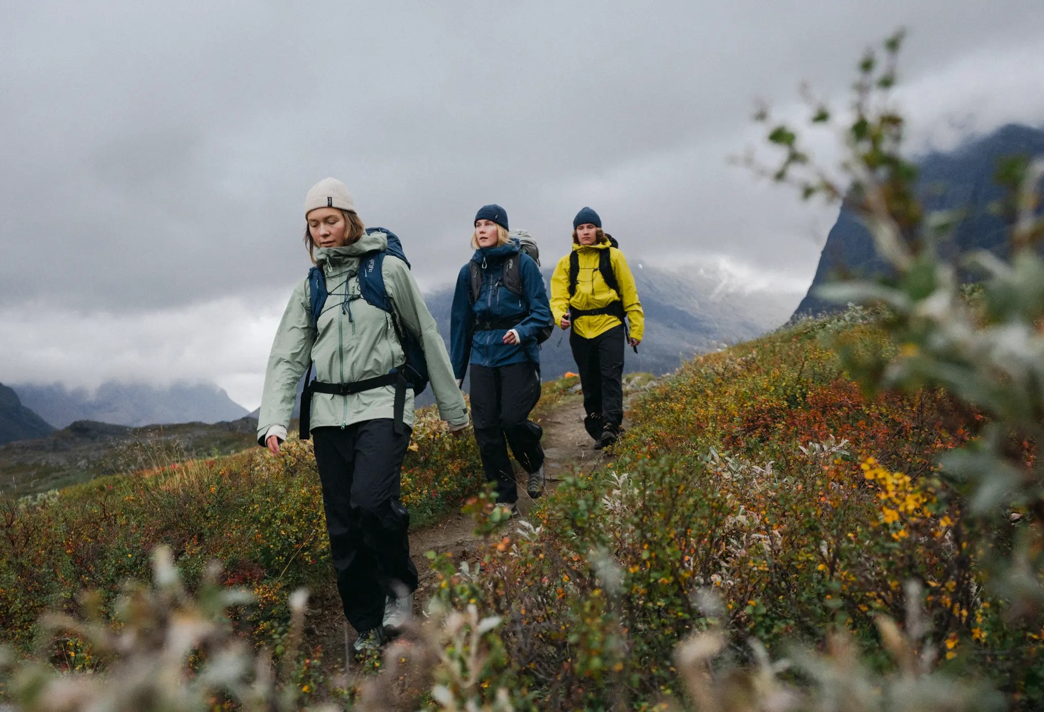 Three hikers on a mountain trail wearing Rab waterproof jackets and packs