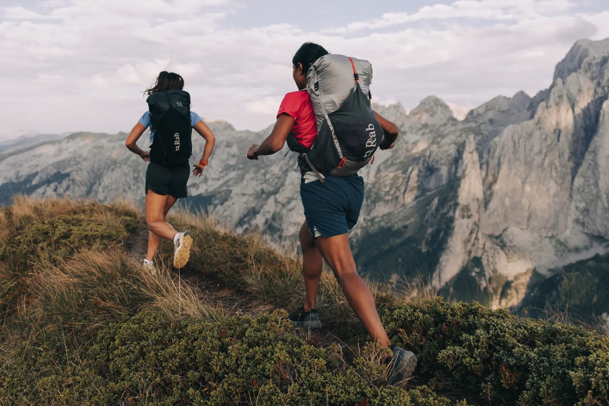 Two hikers running along a mountain ridgeline with Rab packs