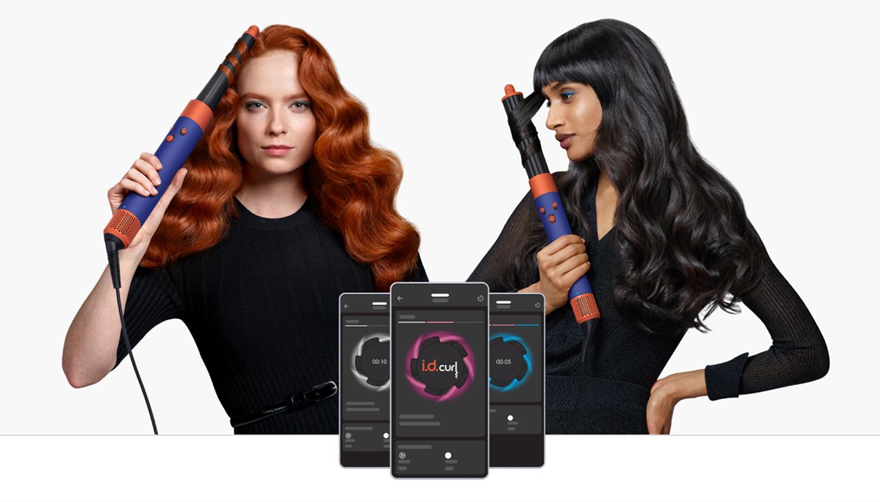 Two models use the Dyson Airwrap i.d. to style their hair. Next to them are three phone screens showing how i.d. curl works.