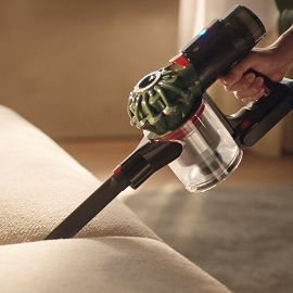La aspiradora Dyson V8 Cyclone se usa con la rinconera para limpiar entre los cojines de un sofá.