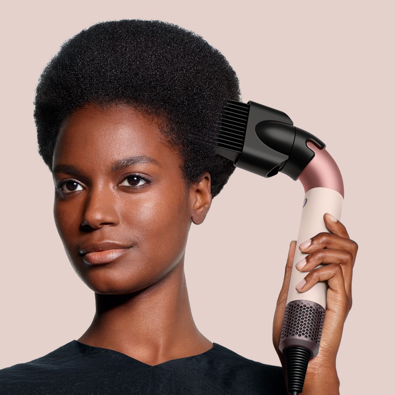 Model holds the Dyson Supersonic Nural hair dryer in Ceramic pink and rose gold.