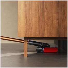 La fregona eléctrica Dyson PencilWash se utiliza para limpiar debajo de un armario bajo.