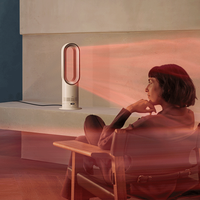 A woman sits in front of her Dyson Hot+Cool HF1 Remote Link Pre-heat heater and cooling fan as it heats the room.