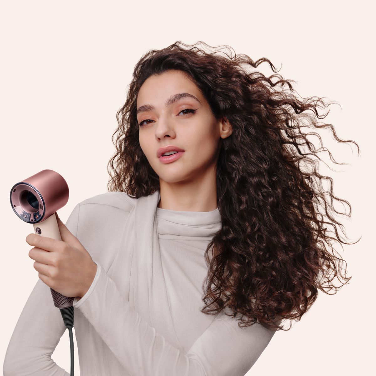 Una modelo con el pelo rizado usa el secador de pelo Dyson Supersonic Travel para secarse el pelo.