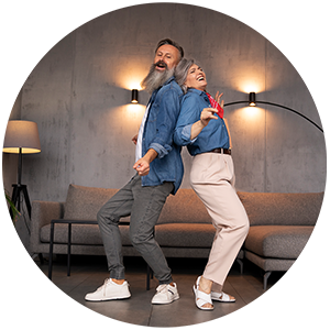 Elderly couple dancing and laughing indoors.