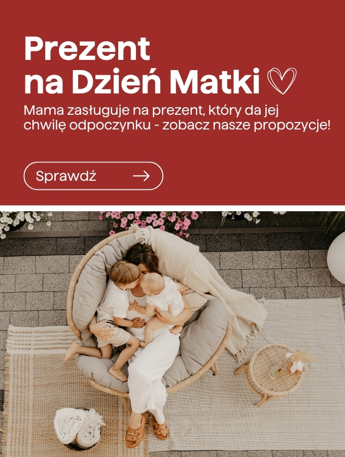 Mother cuddling two young children in a round rattan chair on outdoor rug beneath a Mother's Day banner — cosy family moment