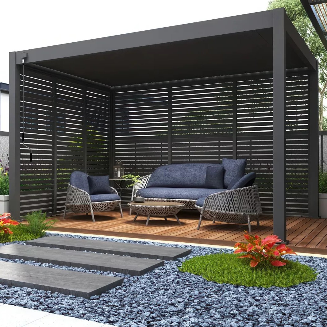 Modern outdoor pergola with grey slatted privacy screens, navy-cushion rattan sofa and chairs on wooden deck, stepping stones and gravel garden