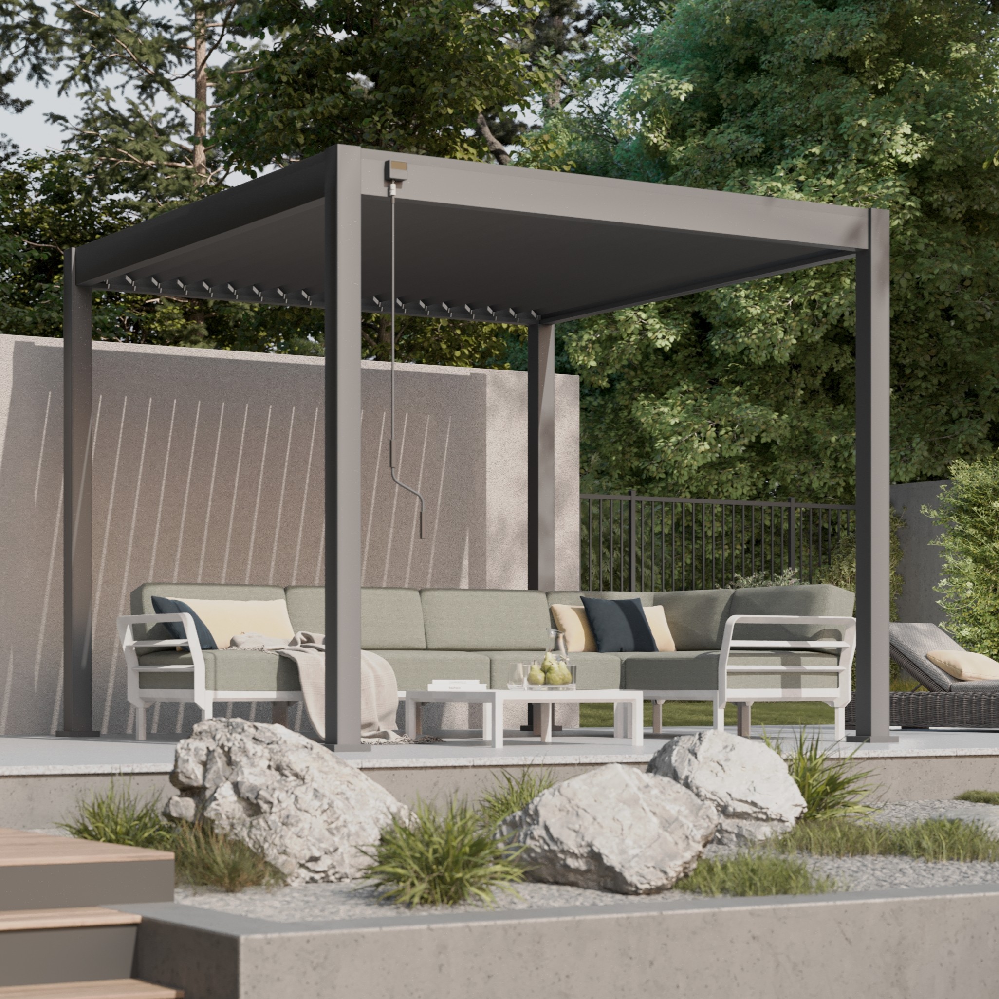 Modern grey pergola with cushioned outdoor sofa and white coffee table on a concrete patio with decorative rocks, plants and trees behind