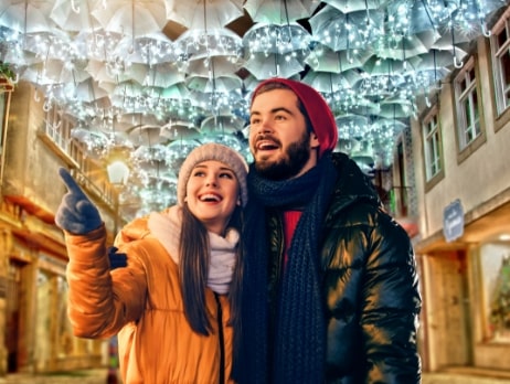 Casal feliz e admirado a olhar para os guarda-chuvas suspensos e iluminados em Águeda