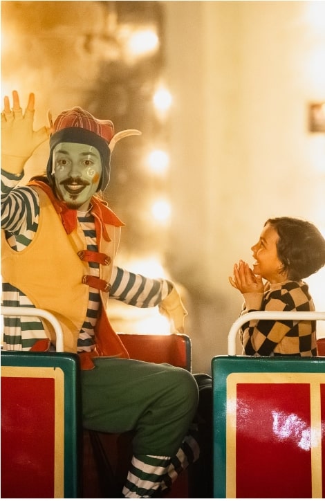 Criança feliz sentada num comboio de Natal a olha para um duende disfarçado