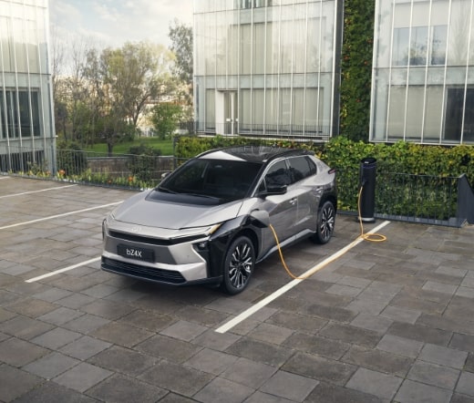 Toyota bZ4X elétrico estacionado e a carregar numa box, num espaço urbano junto a edifícios modernos.