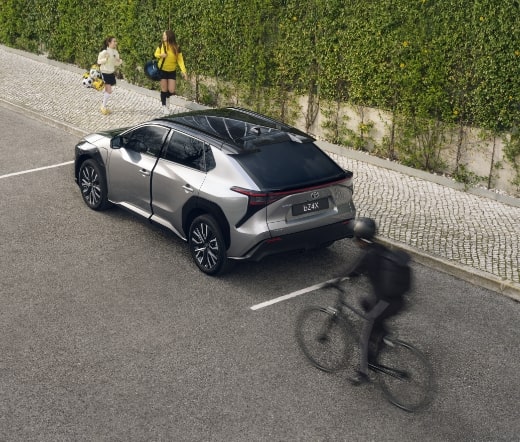 Vista traseira do Toyota bZ4X elétrico a circular na estrada com ciclista ao lado.