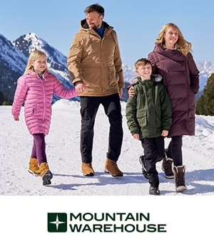 Mountain Warehouse - A family dressed in colorful winter coats walks on a snowy path, surrounded by mountains under a clear blue sky, smiling warmly.