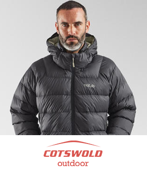 Cotswold Outdoors - Man in a black puffer jacket with a hood looks serious against a gray background.