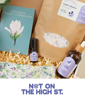 notonthehighstreet: Gift set flat lay featuring a wellness book, essential oil, floral-print card, and bath salts over shredded paper.