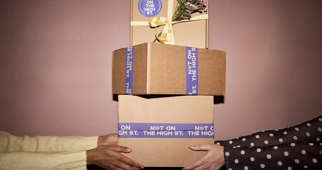 notonthehighstreet: Hands holding a stack of three gift boxes with "Not On The High St." tape. Top box has flowers and a yellow ribbon.