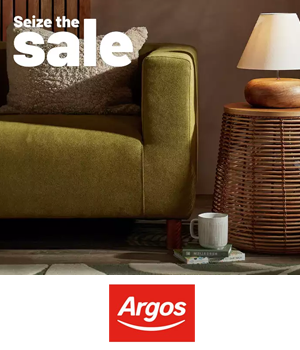 Argos: Cosy living room scene featuring a green sofa, wicker side table with a lamp, and a coffee mug.