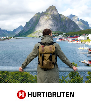 Hurtigruten - Man holding onto railings looking over a town with mountains in the distance