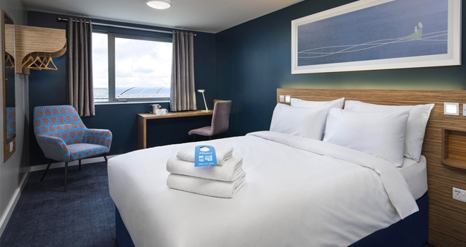 Travelodge - Double bed, desk and open wardrobe in a Travelodge room
