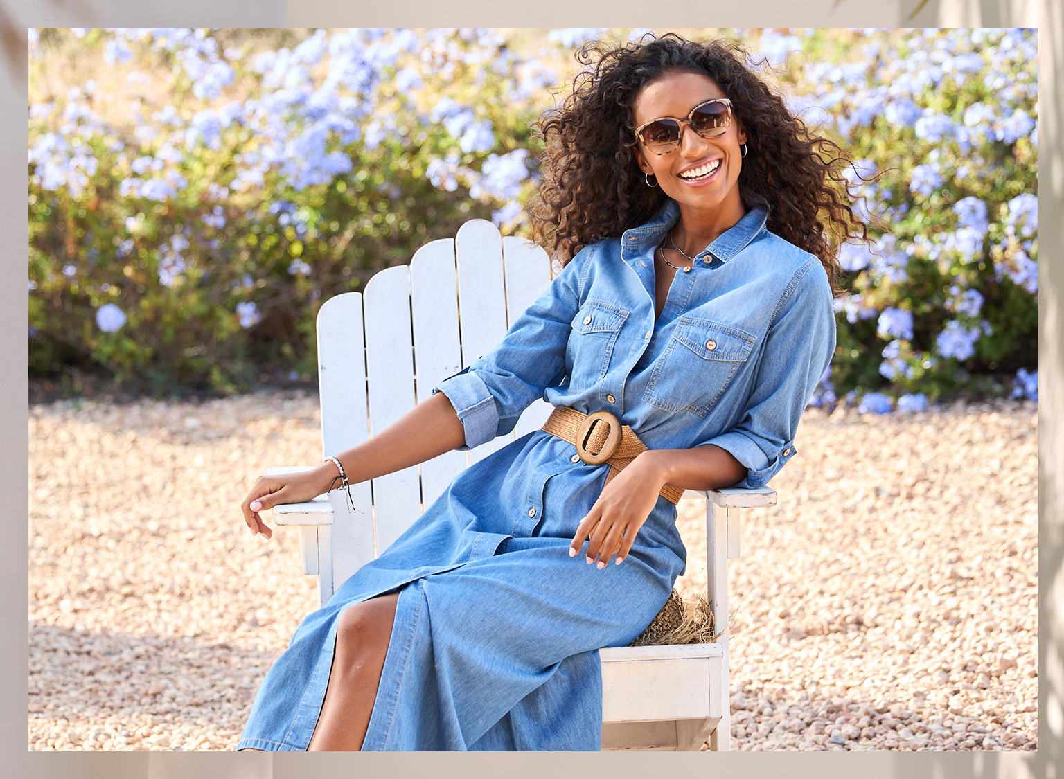  Ein Model sitzt draußen auf einem weißen Stuhl und trägt ein langes Jeanskleid mit Gürtel