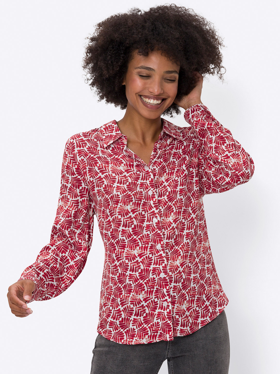 Ein Model trägt eine langärmelige Bluse mit rotem und weißem Blattmuster, dazu graue Hosen, vor weißem Hintergrund.