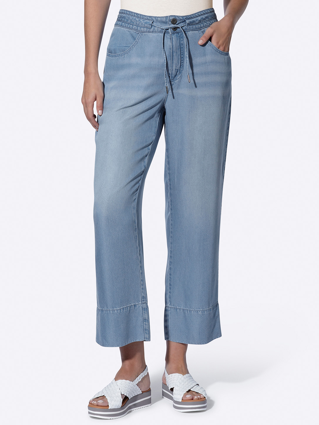 Damenhose aus leichtem Jeansstoff mit weitem Bein, Tunnelzug und Umschlag am Saum, kombiniert mit weißen Sandalen.