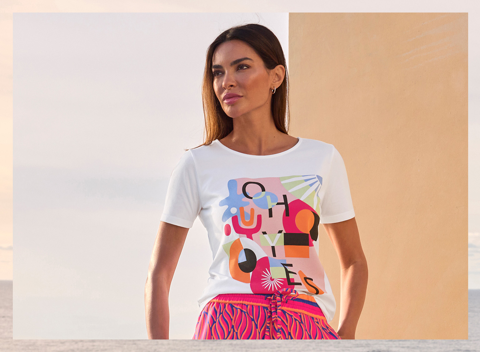  Ein Model trägt ein weißes T-Shirt mit buntem abstraktem Print, kombiniert mit einer pink-roten Hose mit Muster.