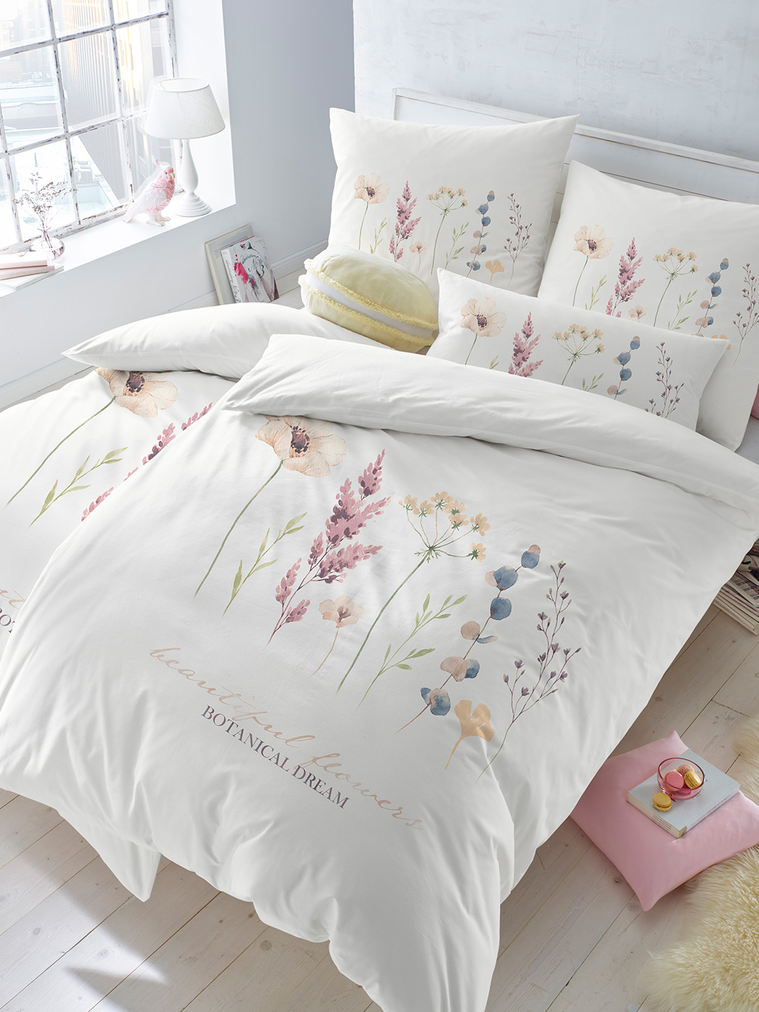 Ein Bett ist mit weißer Bettwäsche mit zarten, bunten Blumenmotiven bezogen. Die Kissen haben das gleiche florale Design. Das Zimmer ist hell und freundlich mit einem Fenster und einem kleinen Nachttisch.