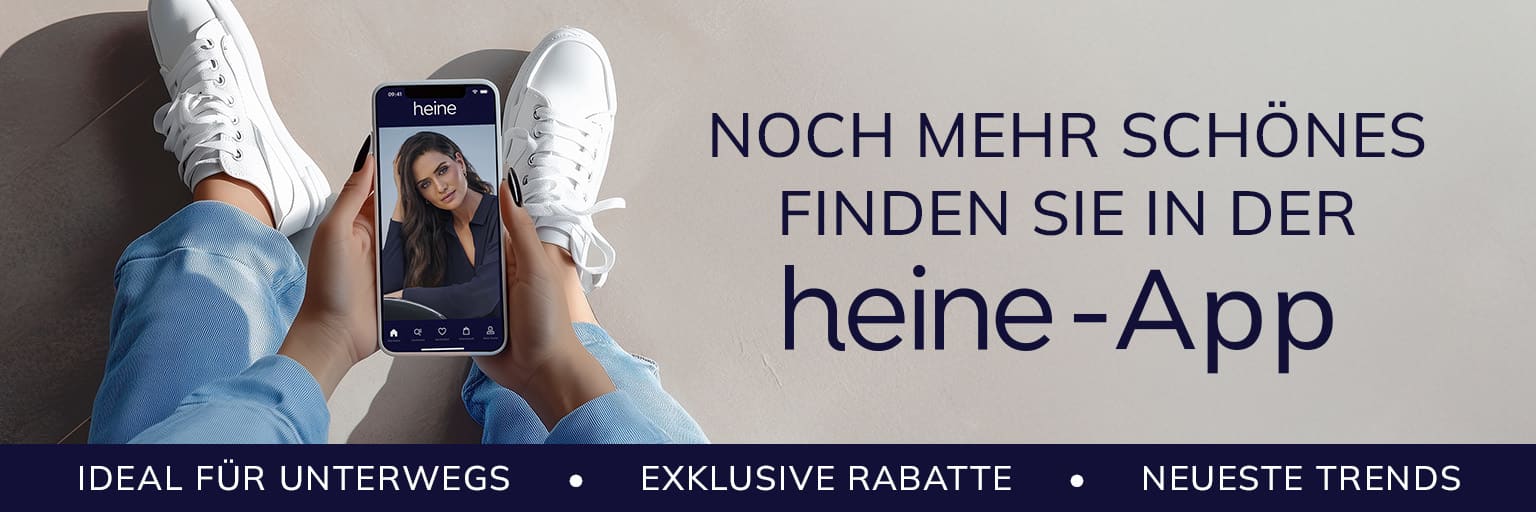 Ein Model hält ein Smartphone mit der heine-App, trägt weiße Sneaker und Jeans. Text: 'Noch mehr Schönes finden Sie in der heine-App. Ideal für unterwegs, exklusive Rabatte, neueste Trends.'