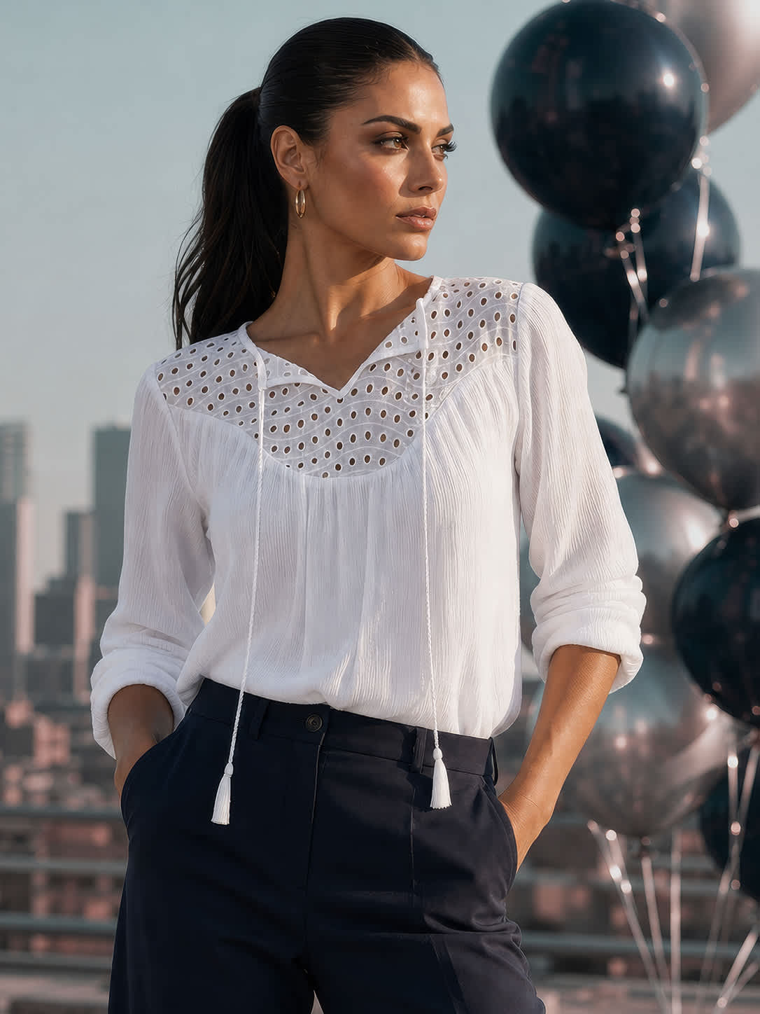 Ein Model mit weißer Bluse und dunkler Hose auf einer Dachterrasse neben schwarzen Ballons.