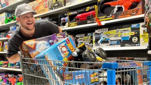 man pushing a shopping cart full of toys down a store shopping aisle
