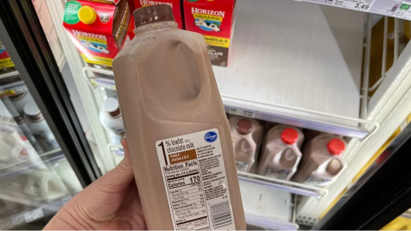a hand holding a gallon of milk in front of a refrigerator