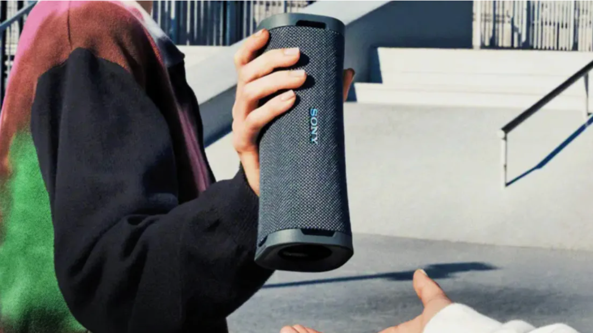 Person with black sweatshirt, holding black Sony speaker in hand