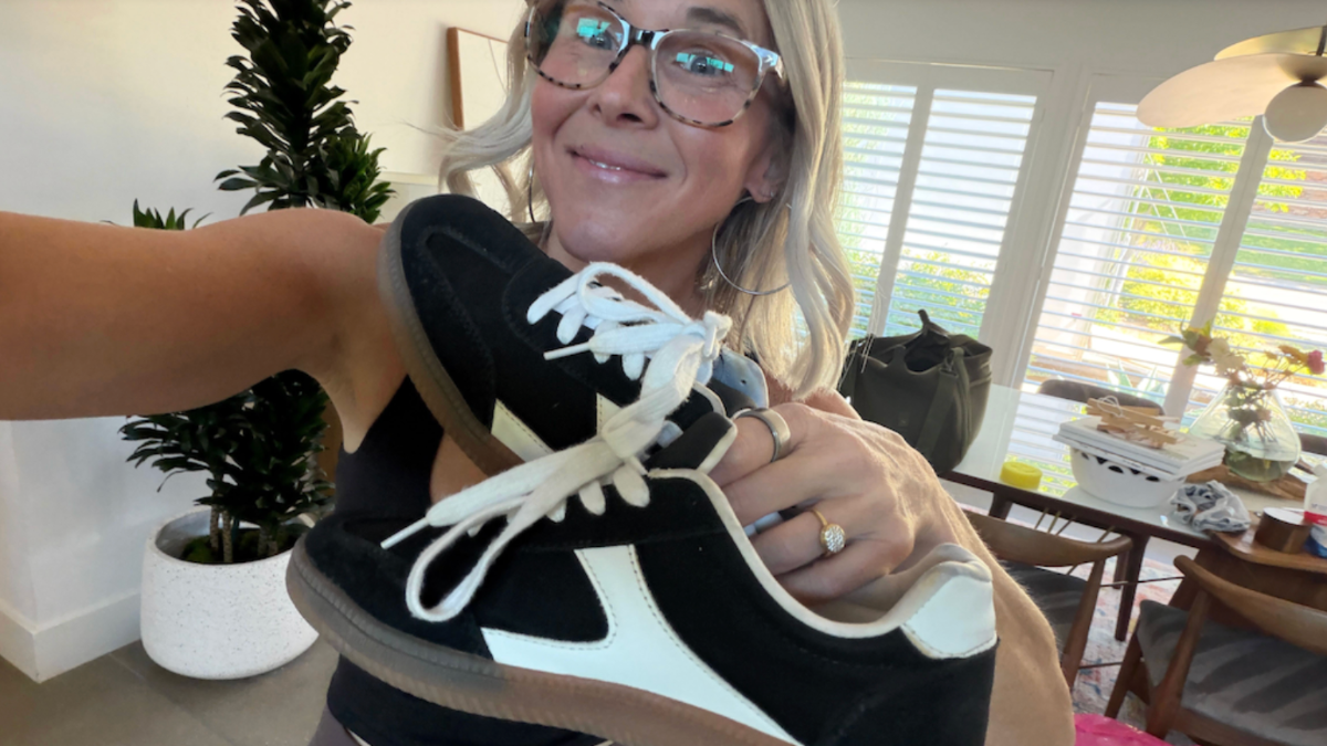 Woman with glasses, holding up a pair of black and white sneakers