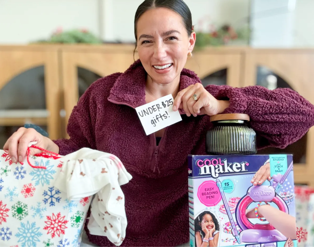 Woman smiling surrounded by gifts and holding Under $25 sign