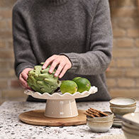 Fehér kerámia tortaállvány és bézs tálak egy pulton