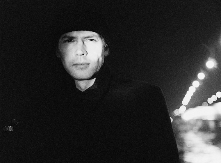 Mustavalkoinen puolikuva kirjailija Ilkka Remeksestä. Remeksen taustalla näkyy kaupungin valoja epätarkkana.