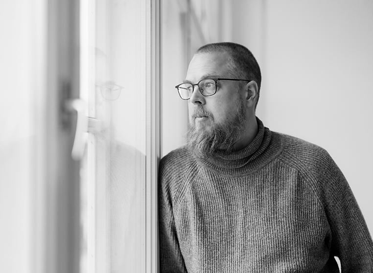 Mustavalkoinen puolikuva kirjailija Tuomas Kyröstä, joka katsoo ulos ikkunasta.