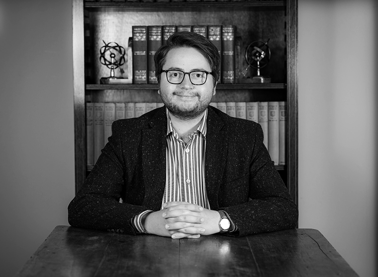 Mustavalkoisessa kuvassa hymyilevä Harry Whittaker istuu työpöydän ääressä kädet ristittyinä eteensä pöydälle. Kuva on otettu suoraan edestäpäin. Whittakerin takana on kirjahylly kirjoineen ja koristeellisine kirjatukineen.