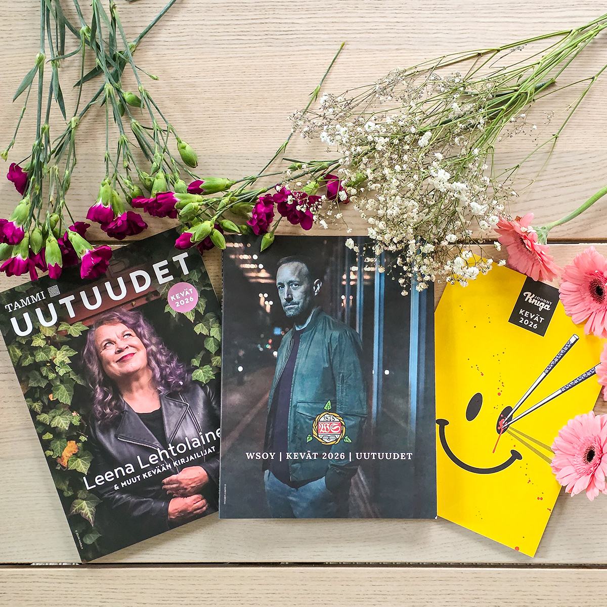 Kevään 2026 kirjakatalogeja ja kukkia pöydällä.