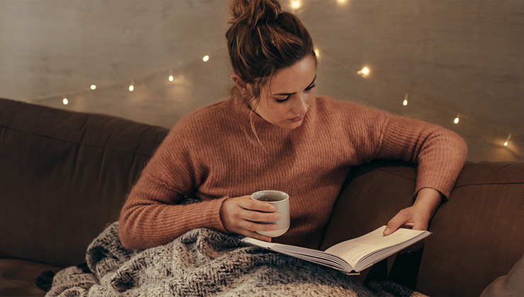 Mevrouw die met een kopje koffie een boek aan het lezen is met lampjes op de achtergrond