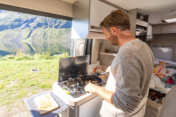 Man aan het koken in een caravan met uitzicht op bergen