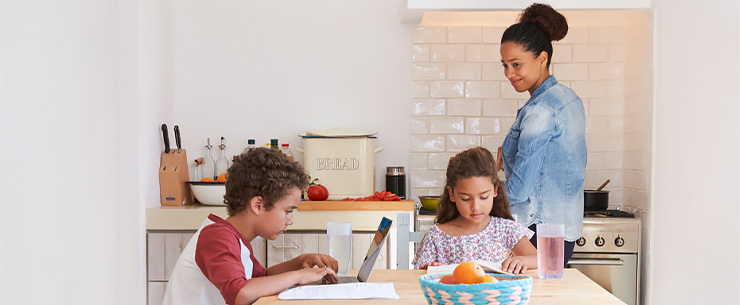 Vrouw met 2 kinderen in de keuken. 1 meisje is aan het lezen en 1 jongen zit op de laptop