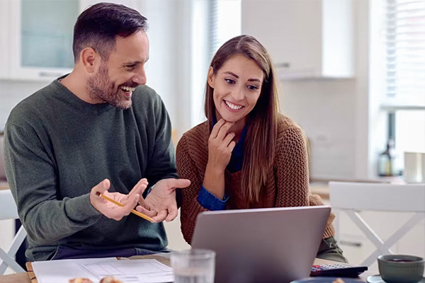 Man en vrouw zitten aan tafel en kijken samen naar een laptop met documenten erbij