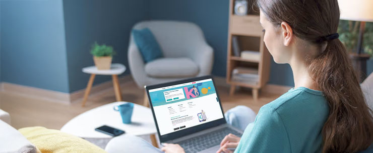 Persoon die op een bank in een woonkamer aan een laptop werkt.