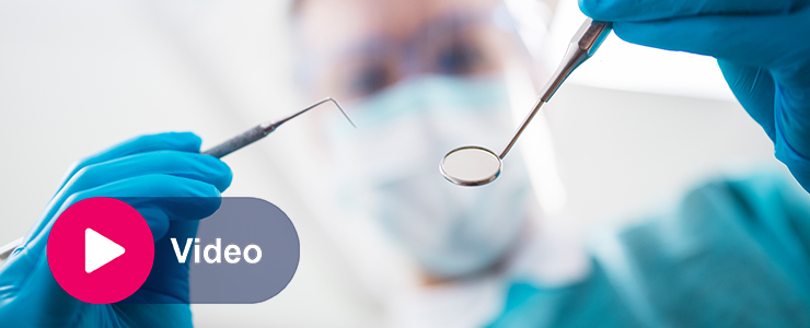 Close-up van een tandarts met mondmasker en handschoenen die een tandheelkundig instrument vasthoudt, met een video-icoon in beeld