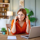 Persoon zit aan een bureau met laptop en telefoneert, met documenten op tafel.