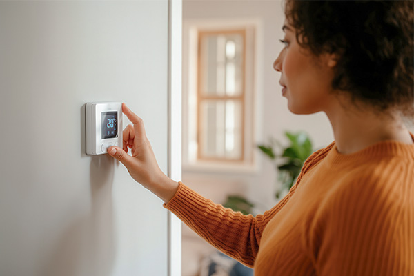 Persoon stelt een digitale thermostaat in die aan de muur is bevestigd.